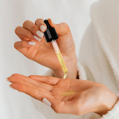 A person holding a dropper with yellow liquid over their palm, ready to apply the Botanical Radiance Oil from LONDONTOWN.