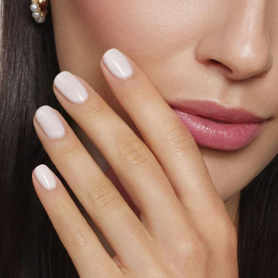 Close-up of a woman's face touching her cheek with a manicured hand. Her smooth skin and glossy lips showcase radiant beauty, enhanced by LONDONTOWN’s Petals & Pearls Set, adding an elegant touch.
