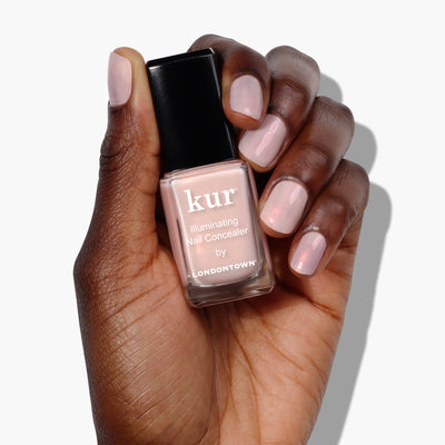 A person with dark skin holds a bottle of Bubble Illuminating Nail Concealer by LONDONTOWN in one hand, displaying their favorite nail polish in a bubblegum pink shade.