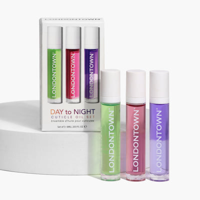 A set of three LONDONTOWN cuticle oils in green, pink, and purple bottles, presented both inside and outside of the packaging box labeled "Day to Night Cuticle Oil Set," designed to nourish dry cuticles and prevent peeling.
