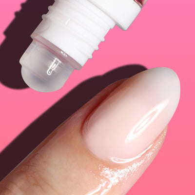 Close-up of LONDONTOWN's Roll & Glow Cuticle Oil - Dragonfruit dispensing a clear liquid on a fingernail, set against a juicy pink background.
