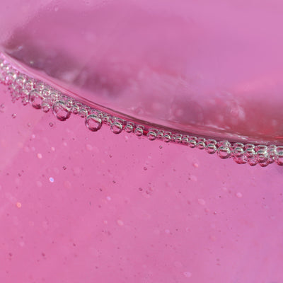 Close-up of the Roll & Glow Cuticle Oil - Dragonfruit by LONDONTOWN, showcasing a pink fizzy liquid with bubbles rising and forming a line near the surface, reminiscent of a juicy hydrator perfect for on-the-go refreshment.