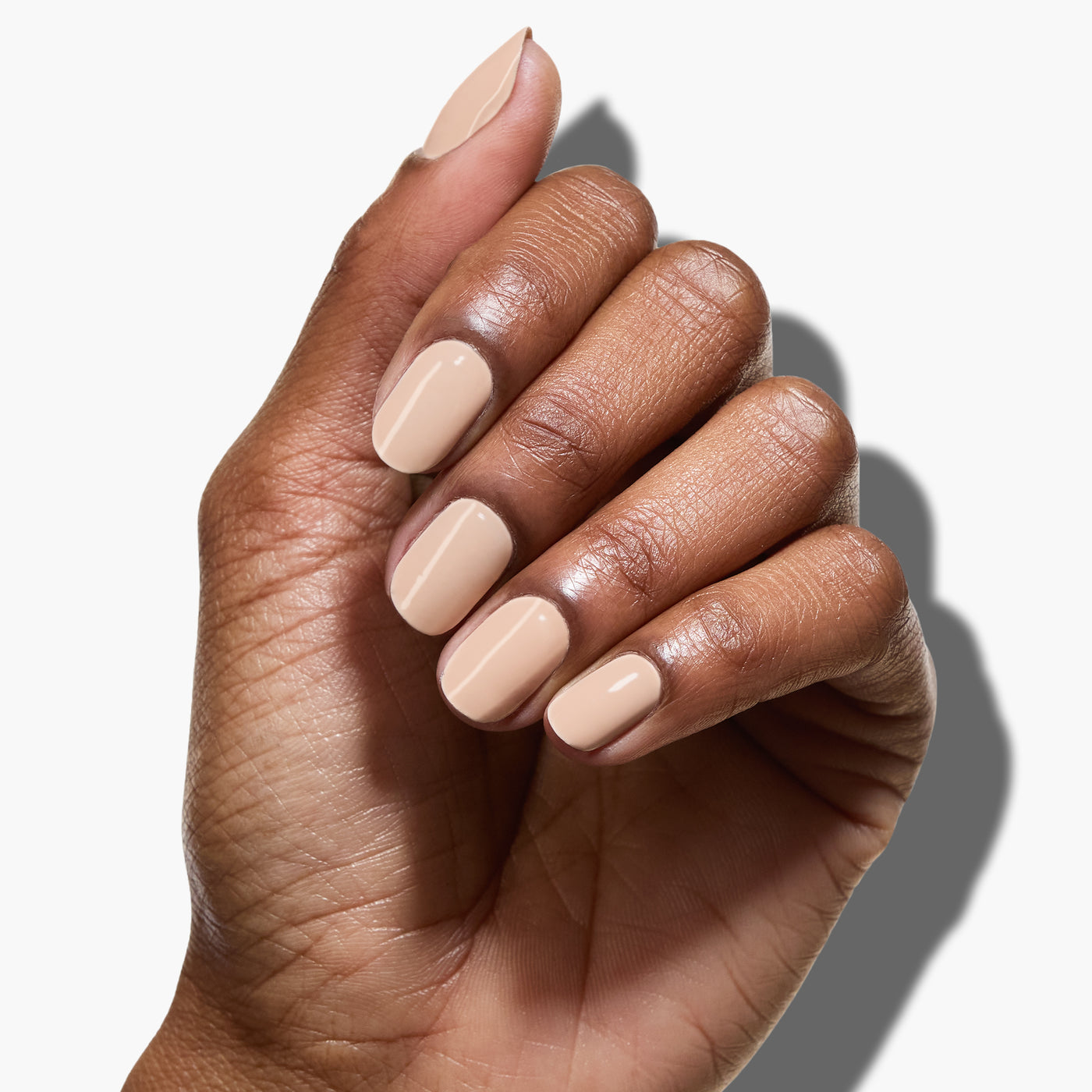 A hand with neatly manicured nails painted in Dusk, a neutral nude beige shade by LONDONTOWN, against a white background.