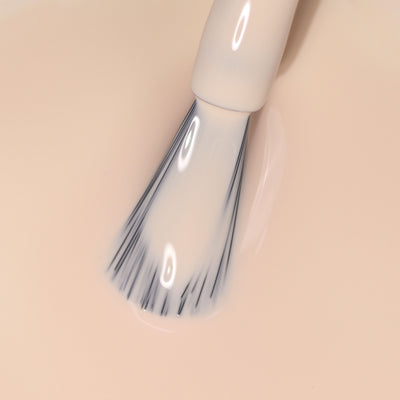 A nail polish brush is immersed in LONDONTOWN's light neutral peach nail polish, Dusk.