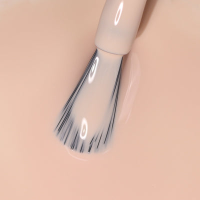Close-up of a LONDONTOWN Dusk (Professional) makeup brush effortlessly applying a beige liquid foundation with a smooth glide over a neutral peach surface.
