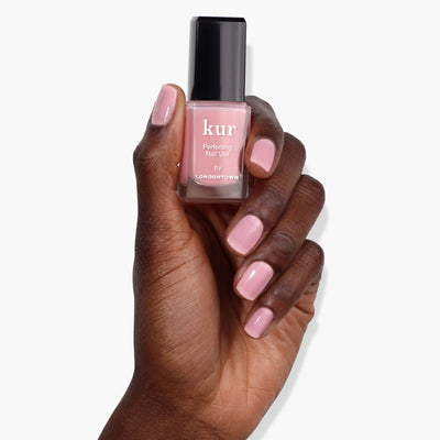 A hand holding a bottle of Perfecting Nail Veil #7 by LONDONTOWN, showcasing nails painted in a power-packed light pink shade.