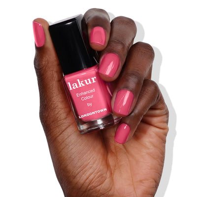 A hand holds LONDONTOWN's Queen of Hearts Galentines Day Set nail polish bottle, with nails painted in matching pink.