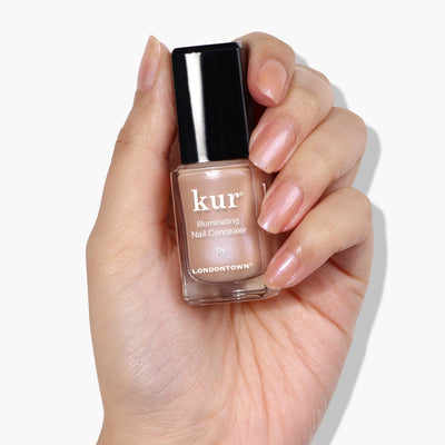 A hand holds a bottle of lustrous beige nail concealer labeled "Bare Illuminating Nail Concealer by LONDONTOWN" against a white background.