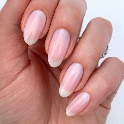 Close-up of a hand displaying neatly manicured nails with LONDONTOWN's Illuminating Nail Concealer, featuring a light pink, glossy finish that brightens dull nails.