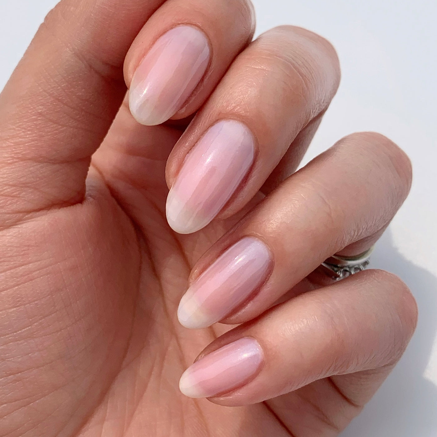 Close-up of a hand with long, oval-shaped nails painted using LONDONTOWN's Pink Illuminating Nail Concealer, showcasing an elegant, glossy, milky white finish.
