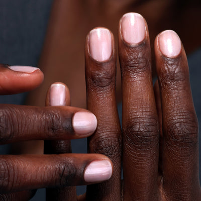 A close-up of hands with neatly trimmed nails painted in a light pink polish, enhanced by LONDONTOWN's Quartz Illuminating Nail Concealer for that flawless finish.