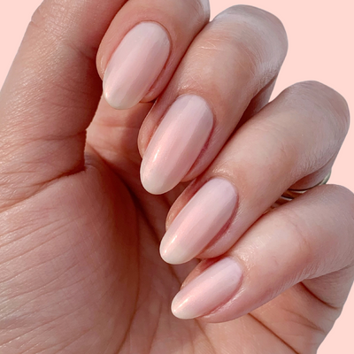 A hand with almond-shaped nails, polished with LONDONTOWN's Bubble Illuminating Nail Concealer in bubblegum pink, displayed against a pale background.