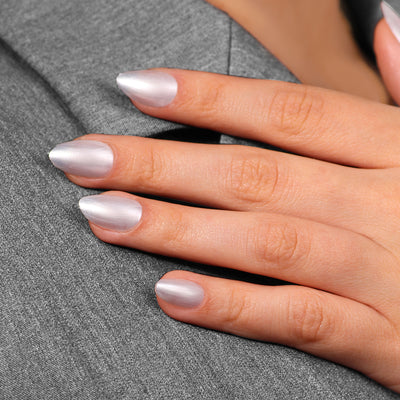 Close-up of a hand against a grey fabric with long, manicured nails painted in the shimmering, chrome silver color of LONDONTOWN's Powder.