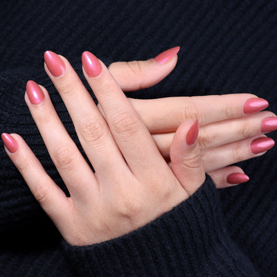 Close-up of crossed hands with long, almond-shaped nails painted in LONDONTOWN's rose-pink shade named Slopeside, wearing a dark, ribbed sweater.