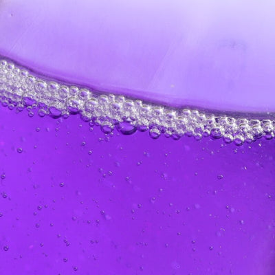 A close-up of the Nighttime Cuticle Quench - Lavender by LONDONTOWN reveals a purple liquid with numerous small bubbles forming a foamy layer along the surface, ideal for soothing cuticle treatment.