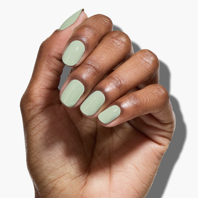 A hand with short, neatly manicured nails painted in LONDONTOWN's Lichen, a calming pale green shade akin to white sage.