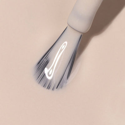 Close-up of LONDONTOWN's Linen makeup brush with white bristles applying a creamy, light beige foundation onto a smooth surface, creating a natural and breezy finish.