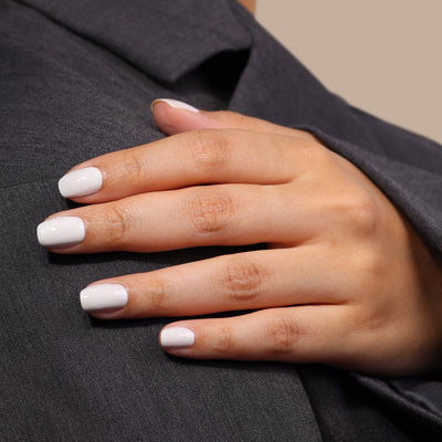 Close-up of a hand with neatly manicured, London Fog (Professional) crisp white nails by LONDONTOWN resting on a cool grey fabric surface.