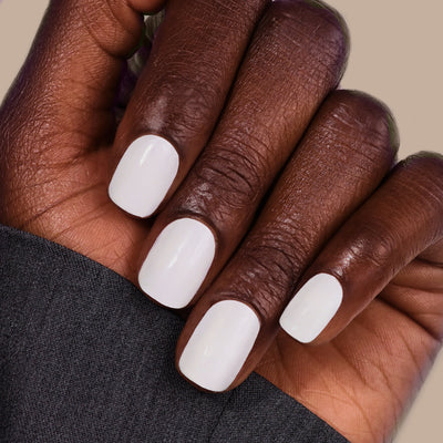 A hand with dark skin tone displaying manicured nails painted in LONDONTOWN's London Fog, partially covered by a cool, dark fabric.