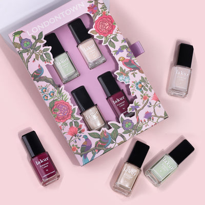 A set of six "Spring Fling Lakur" nail polish bottles from LONDONTOWN are arranged on a pink surface, with one bottle placed in a decorated box, reminiscent of a bouquet of vibrant colors perfect for gifting to mom.