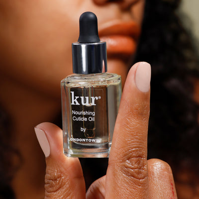 A person holding a bottle of LONDONTOWN's Nourishing Cuticle Oil with a dropper, focusing on the label that emphasizes this essential cuticle care product.