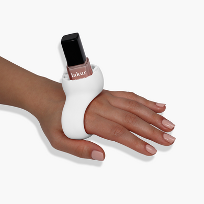 A hand with manicured nails wearing the LONDONTOWN Bottle Service Polish Holder on the back of the hand, holding a bottle of pink nail polish, showcasing an easy manicure perfect for both manis & pedis.