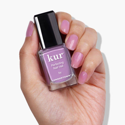 A hand holding a bottle of pink nail polish labeled "Perfecting Nail Veil #9 by LONDONTOWN," with nails painted in the same shade. This power-packed formula adds a hint of color while providing essential care for your nails.