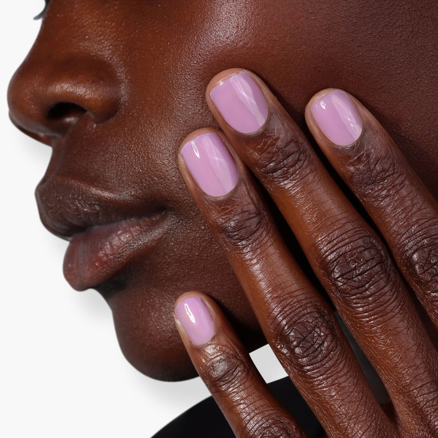 Close-up image of a person touching their cheek with fingers painted in Perfecting Nail Veil #9 from LONDONTOWN, showcasing a hint of light purple color and care.
