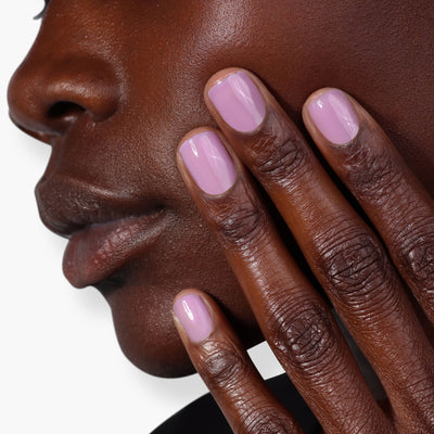 Close-up image of a person touching their cheek with fingers painted in Perfecting Nail Veil #9 from LONDONTOWN, showcasing a hint of light purple color and care.
