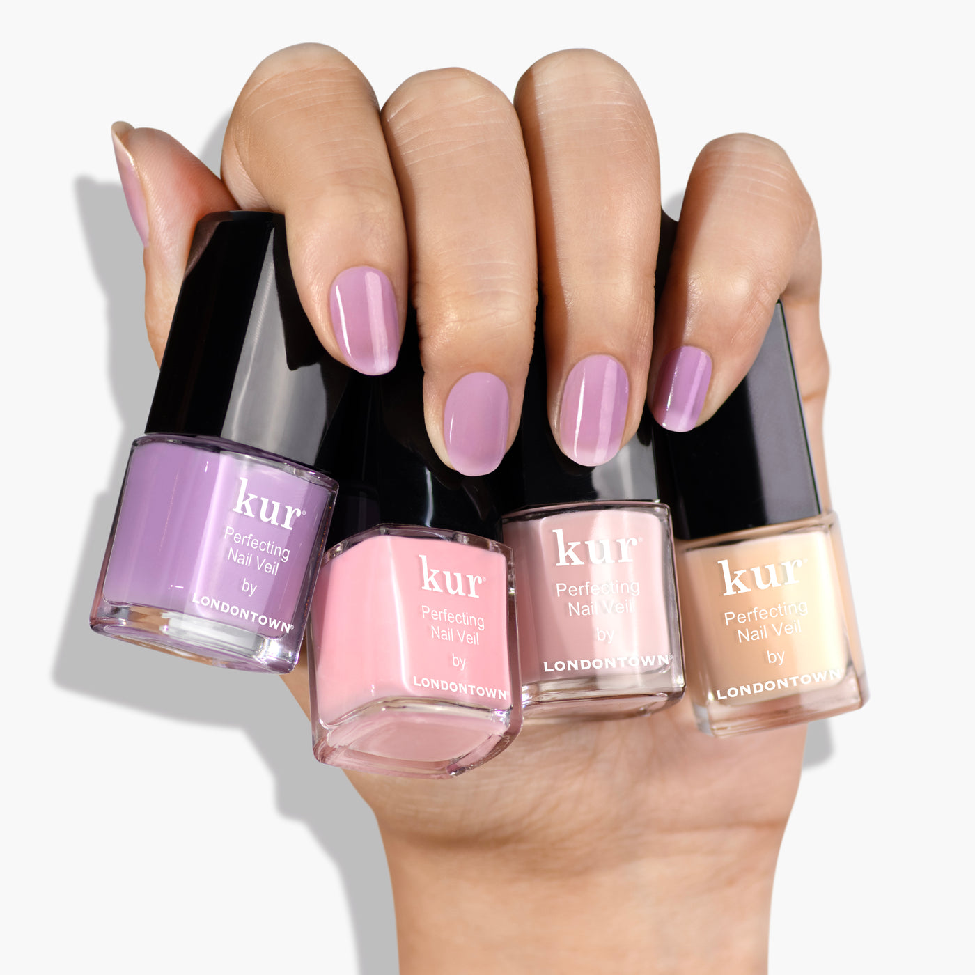 A hand with manicured nails holds four bottles from LONDONTOWN’s Perfecting Nail Veil Mini Set in various shades of pink and beige, capturing sheer perfection.