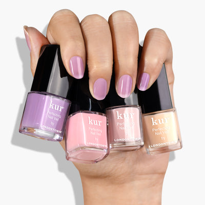 A hand with manicured nails holds four bottles from LONDONTOWN’s Perfecting Nail Veil Mini Set in various shades of pink and beige, capturing sheer perfection.