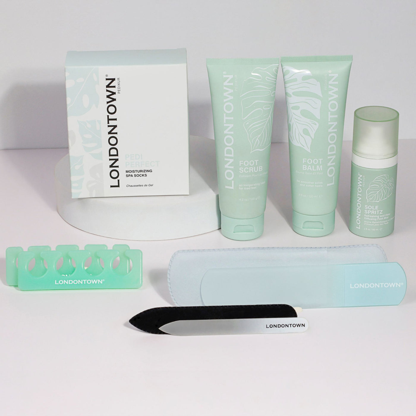 Introducing the Pedi Discovery Set by LONDONTOWN, a luxurious pedicure collection featuring foot care favorites: Pedi Perfect Moisturizing Sock, Foot Scrub, Foot Balm, Sole Spritz, a toe separator, a nail file, and a foot file.