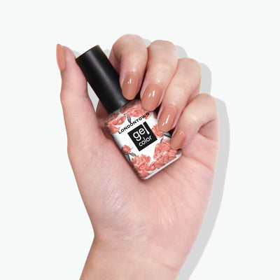 A hand holding a nail polish bottle labeled "Savanna" from LONDONTOWN, adorned with a pink floral design. Nails are painted in a matching, muted nude shade.