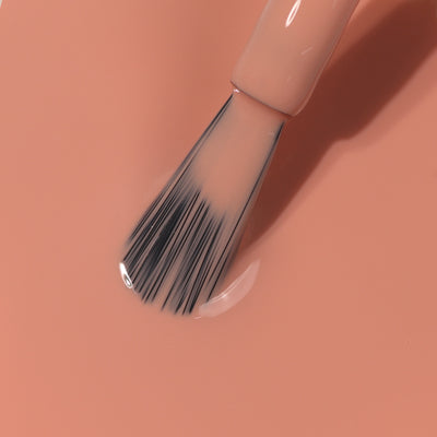 Close-up of a Savanna nail polish brush with black bristles on a light peach background, dipped in LONDONTOWN's muted matte liquid nail polish.