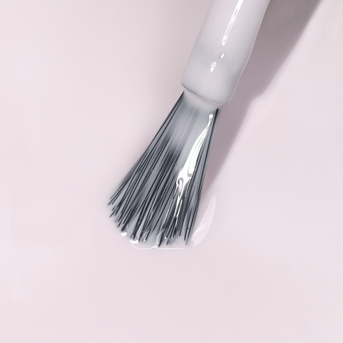 Close-up of the Ski Bunny nail polish brush from LONDONTOWN, with gray bristles applying clear, pink-tinted cream polish on a light surface.