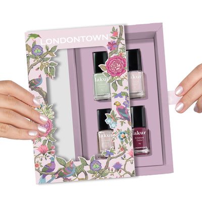Two hands holding an opened LONDONTOWN Spring Fling Lakur Set with three bottles of pastel nail polish, surrounded by floral and bird-themed packaging, perfect for mom.