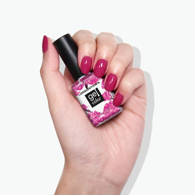 A hand with manicured nails holds a bottle of gel nail polish labeled "Teeny 'Kini" by LONDONTOWN, featuring a floral design on the bottle. The nail polish color, reminiscent of fruity sangria, perfectly matches the shade on the nails.