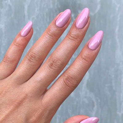 Long, almond-shaped nails flaunt a glossy pink hue using LONDONTOWN's Flash Dry Top Coat, set against a gray backdrop.