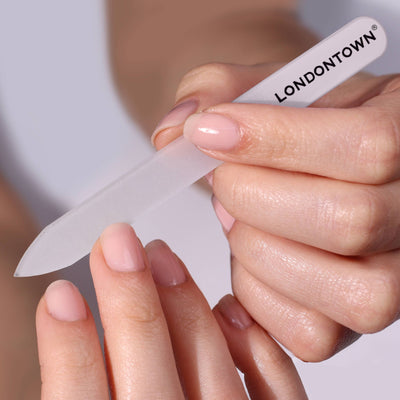 Close-up of hands effortlessly using a LONDONTOWN Glass Nail File - White on fingernails, ensuring a damage-free experience, with a neutral background.