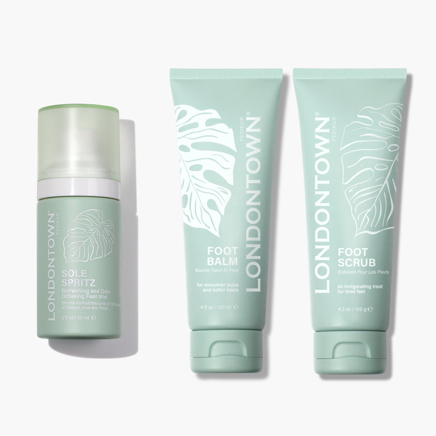 Three green Fast Bundle skincare products—Sole Spritz (hydrating foot essence), Foot Balm (nourishing foot cream), and Foot Scrub (exfoliant cream for feet)—comprise the Sole Essentials Trio, all placed against a white background to pamper your feet with ultimate rejuvenation.