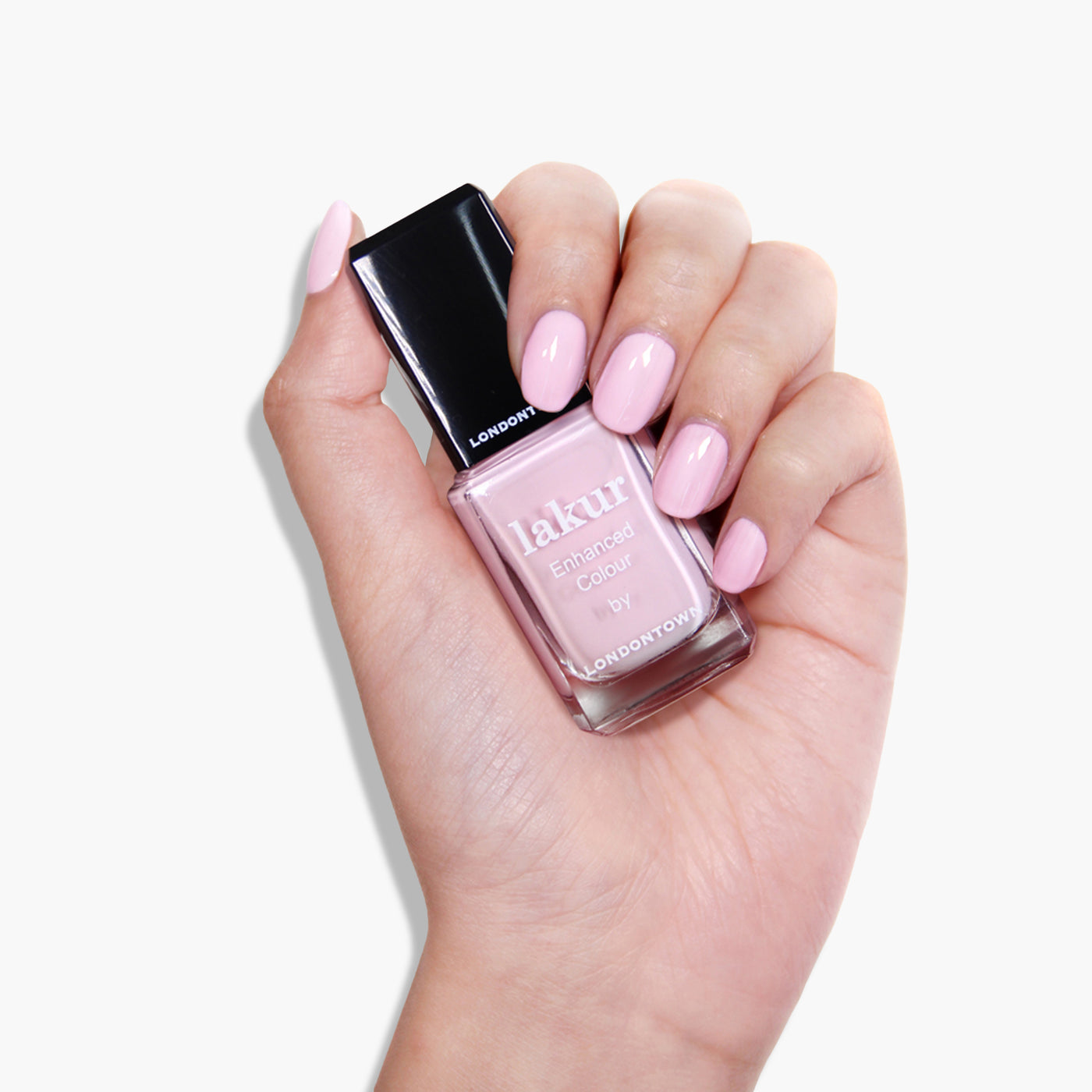 A hand holding a bottle of LONDONTOWN Afternoon Tea nail polish with light pink crème painted nails, making it everyone's cup of tea.