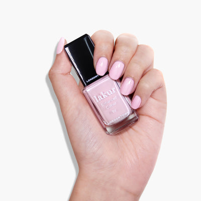 A hand holding a bottle of LONDONTOWN Afternoon Tea nail polish with light pink crème painted nails, making it everyone's cup of tea.