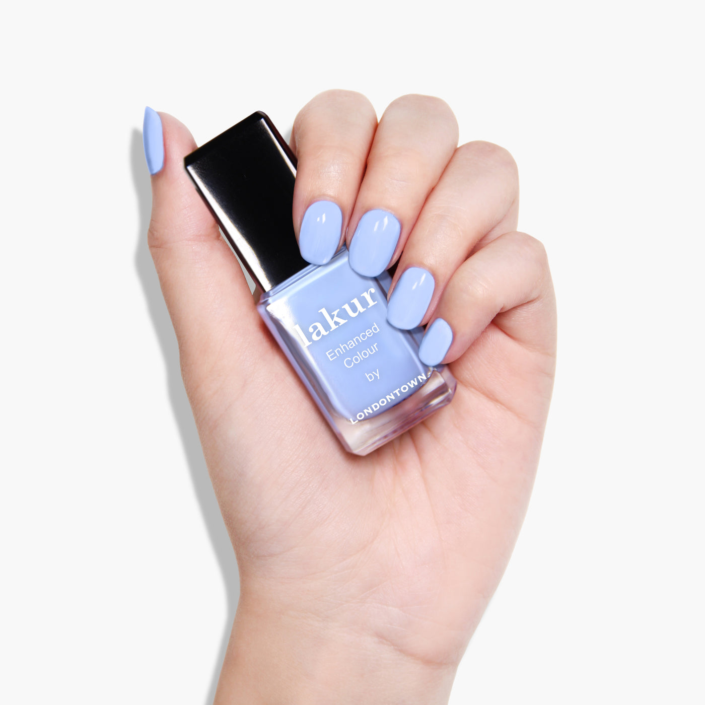 A hand with manicured nails painted a cool blue tone holds a bottle of light blue, 16+ Free nail polish with a black cap, labeled "Amalfi Love by LONDONTOWN," showcasing its vegan, cruelty-free formula.