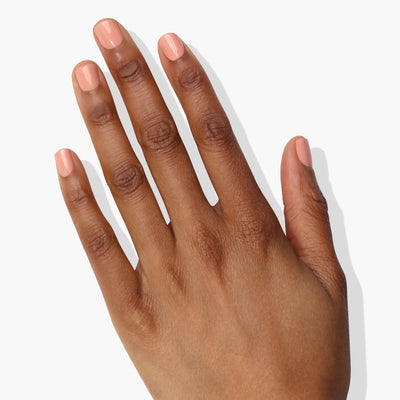 A hand with neatly trimmed fingernails painted in LONDONTOWN's Amber Lights (Professional), a light peach color reminiscent of a soft sunset, positioned against a plain white background.