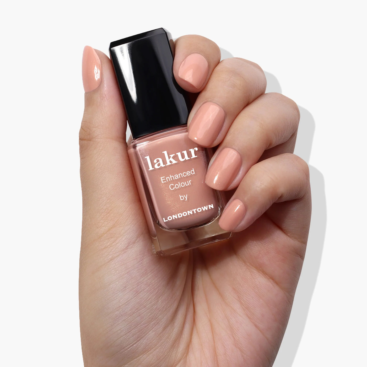A hand holding a bottle of Amber Lights (Professional) by LONDONTOWN nail polish in a sunset peach color.