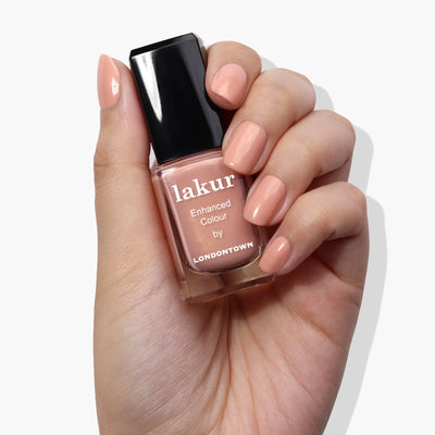 A hand holding a bottle of Amber Lights (Professional) by LONDONTOWN nail polish in a sunset peach color.