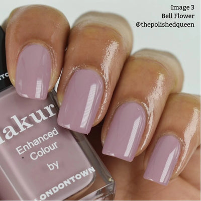 A close-up of a hand with neatly manicured nails painted in a dusty pink shade. The person holds a bottle of LONDONTOWN "Bell Flower (Professional)" nail polish, matching the elegant hue perfectly.
