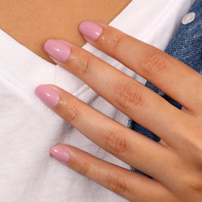 A hand adorned with neatly manicured Berry Nude nails by LONDONTOWN rests gently on a white fabric, with a snippet of blue material resembling luscious blueberries visible in the background.