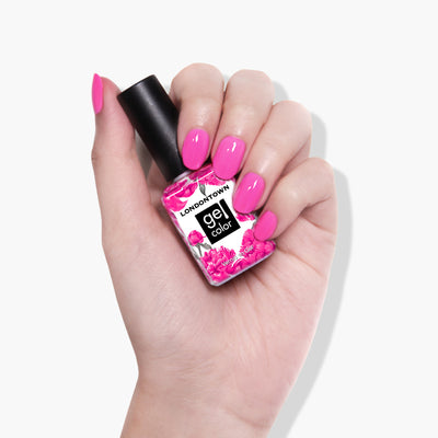 A hand holding a pink nail polish bottle labeled "LONDONTOWN Berry Punch"; the nails, painted with bold fuchsia polish, shimmer under UV/LED light.