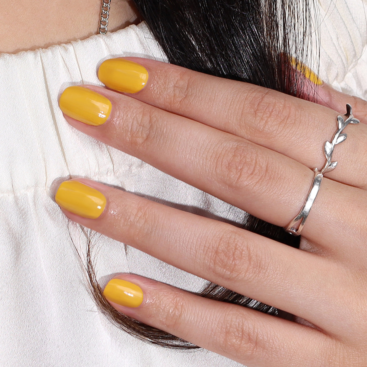 A hand with cheerful Daisy Chain canary yellow-painted nails, adorned with a LONDONTOWN silver ring featuring a twig design, rests on a white fabric.